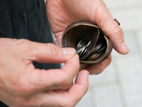 一雙手拿著一個深棕色皮革製的圓形零錢包，拉鍊部分打開，露出裡面裝有各種硬幣。