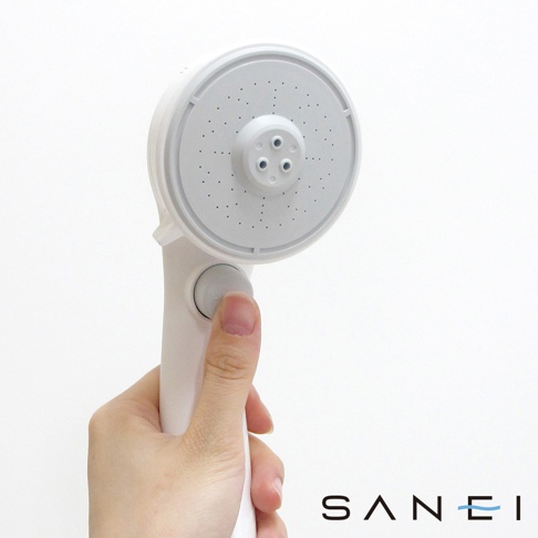 手持白色SPA沙龍省水蓮蓬頭，蓮蓬頭為圓形，設有多個小噴孔，中間有三個較大的出水孔。蓮蓬頭下方有圓形按鈕，拇指正在按下。