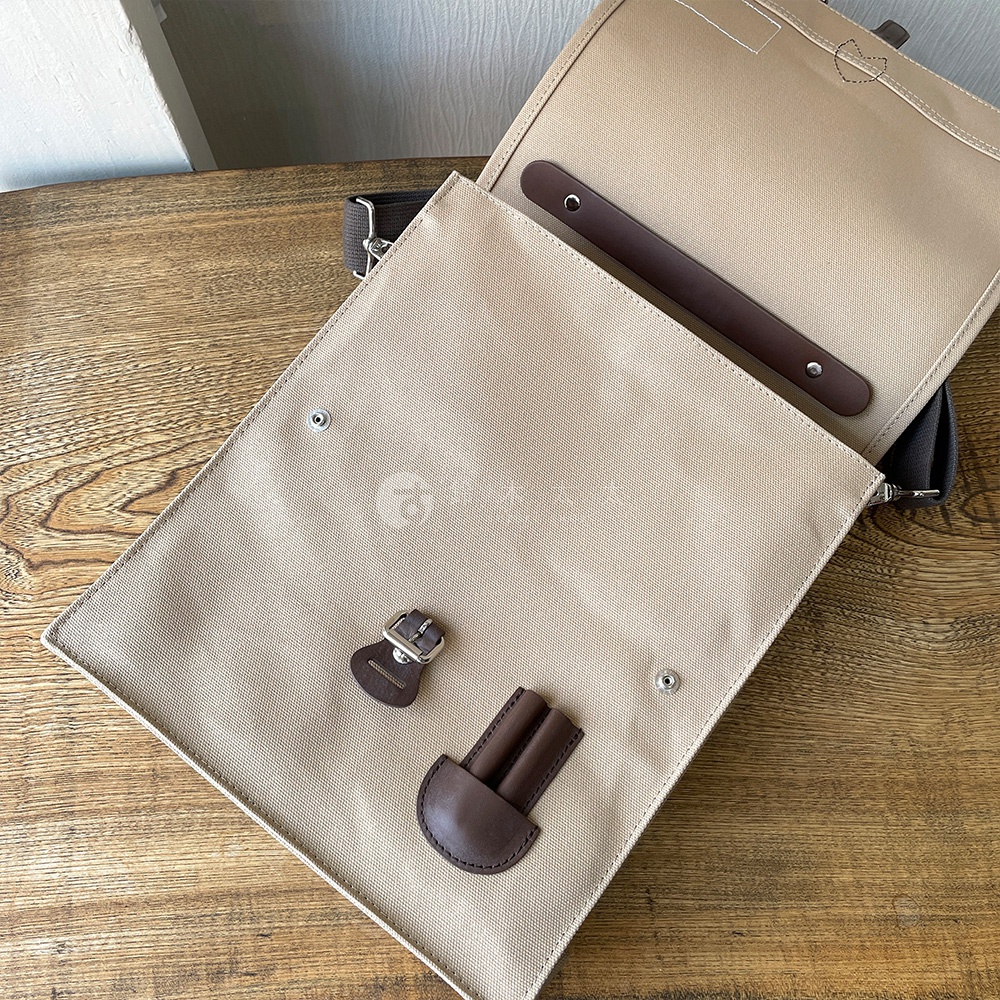 米色純棉帆布三用直式側背包，打開翻蓋，內有深棕色皮革飾邊及金屬扣環，整體設計簡潔。