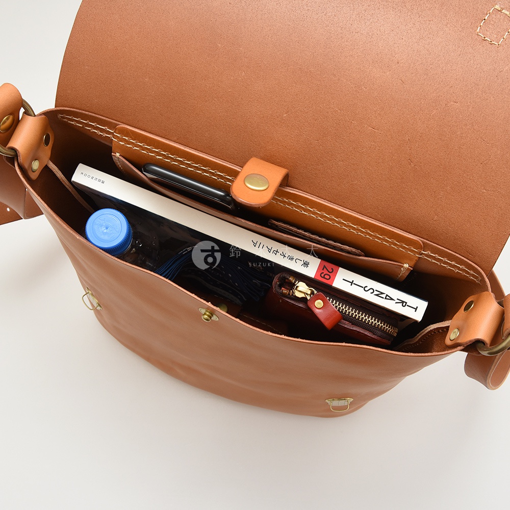 HERZ 職人手作皮革雙扣旅行郵差包內部，可見一本書籍、手機、水瓶及零錢包