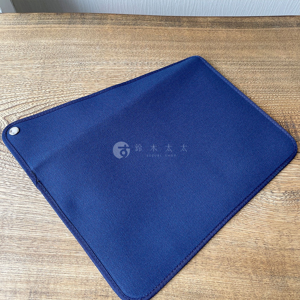 深藍色純棉帆布平板收納包，有銀色按扣，邊緣縫線清晰，置於木紋桌面上。