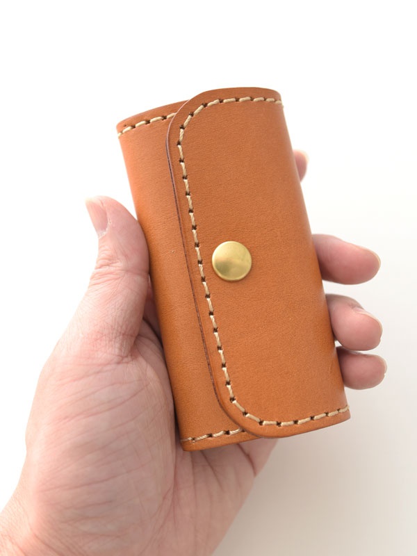 手持一個棕色皮革鑰匙包，包身有縫線裝飾，並有一個金色按扣。