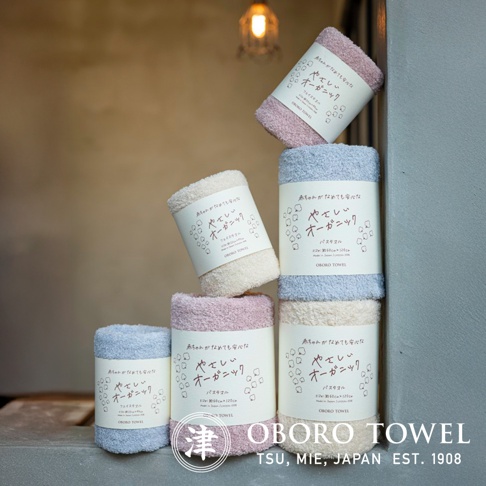 堆疊的有機棉浴巾，呈現粉紅色、淺藍色和米白色，質地柔軟，帶有日文標籤。