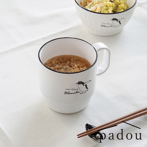白色馬克杯中盛裝著熱騰騰的泡麵，杯身印有手繪風企鵝插圖與 Blanche 字樣。桌面上另擺放著一個盛裝沙拉的碗以及一對架在可愛企鵝造型筷架上的木質筷子，整體呈現出清新簡約的日系用餐氛圍。