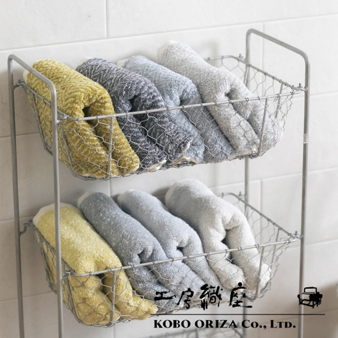 两层金属网篮中整齐叠放着 SUFFICE 棉麻混纺毛巾，毛巾颜色包括芥末黄、深灰、浅灰和浅蓝色，材质触感柔软蓬松。