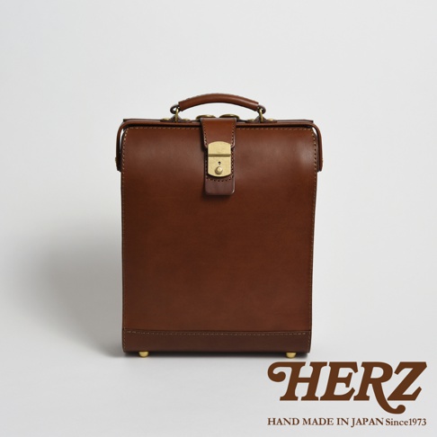 棕色皮革手作杜勒斯商務後背包，配有金色金屬鎖扣、手提把和四個底部支撐腳。