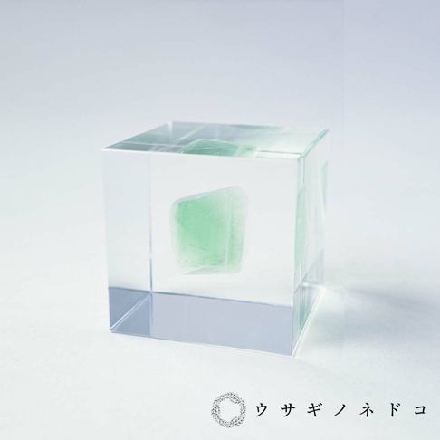 透明立方體內嵌有綠色螢石礦石，礦石呈不規則塊狀，表面有結晶紋理，光線穿透立方體和礦石，營造出朦朧感。