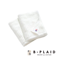 兩條白色純棉毛巾，表面有直條紋理，其中一條毛巾角落繡有「B-PLAID」品牌標誌，標誌由紅、藍、白色塊組成。