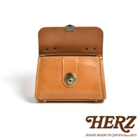 職人手作皮革迷你手提包，採用天然皮革製作，呈現溫潤的焦糖棕色。包款正面有一個金屬旋轉鎖扣，掀蓋式設計，縫線精緻，整體風格簡約而復古。