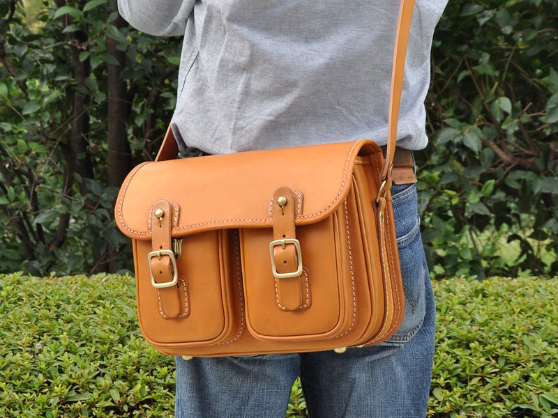 職人手作皮革皮扣直式單肩包，採用天然棕色皮革製作，配有兩個前袋和金屬釦帶，設計簡約實用。
