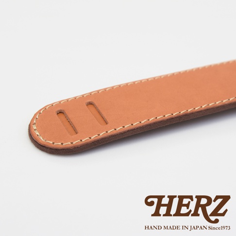職人手作皮革Big肩墊，採用天然棕色皮革，雙層結構，邊緣以米白色縫線車縫，頂部有兩個長方形開孔，下方有品牌HERZ標誌。