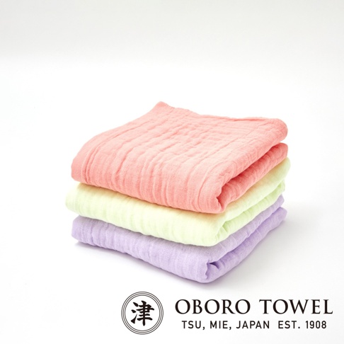 三層紗純棉寶寶裹身毯，堆疊展示，由上而下分別為珊瑚粉、淺綠與淡紫色，材質柔軟，紋理清晰。