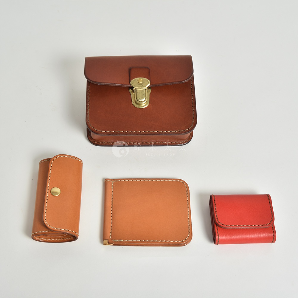 展示了四件皮革製品：一個棕色方形腰包，配有黃銅釦；一個淺棕色捲式鑰匙包，配有黃銅釦；一個淺棕色皮夾；以及一個紅色零錢包。