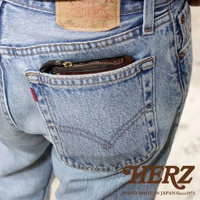 職人手作皮革小型雙折短夾，深咖啡色，置於牛仔褲後口袋，露出金色拉鍊。