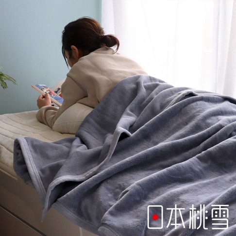 舒眠雙面四季毯，灰色絨毛材質，質地柔軟，蓋在床上，一位女子正蓋著毯子閱讀。