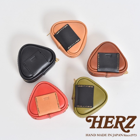 五款職人手作皮革三角飯糰造型小物收納包，顏色包含黑色、棕色、橘色、紅色及綠色。每個收納包均由皮革製成，並飾有黑色皮革片和縫線細節，造型獨特可愛。