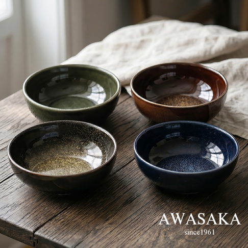 擺放在木質桌面上的一組四個 AWASAKA 品牌陶瓷寬口碗，碗身呈現深綠、深棕、帶有金粉感的深褐與深藍色調，表面擁有細緻光澤，後方襯托著柔軟的淺色棉質布料，整體展現簡約質樸的日式工藝美學。