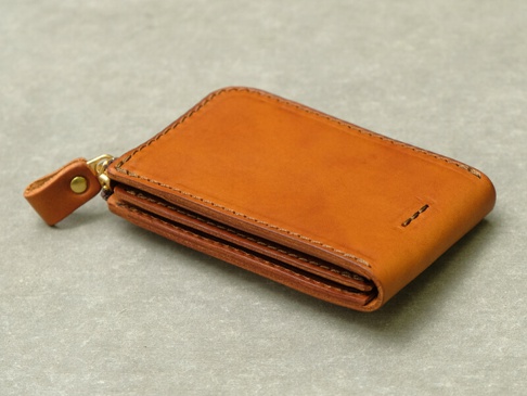 一個棕褐色皮革製成的拉鍊式卡片鑰匙包，展示了精緻的縫線細節、黃銅拉鍊和皮革拉環。