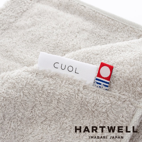 淺灰色 CUOL 品牌標籤縫製於柔軟、絨毛感的美髮毛巾上，毛巾質感細緻，觸感柔順，側面可見 HARTWELL IMABARI JAPAN 字樣。