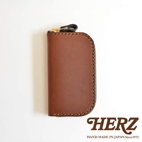 職人手作棕色皮革橢圓形拉鍊鑰匙包，附有黃銅拉鍊頭與皮革拉環，整體呈現復古質感。