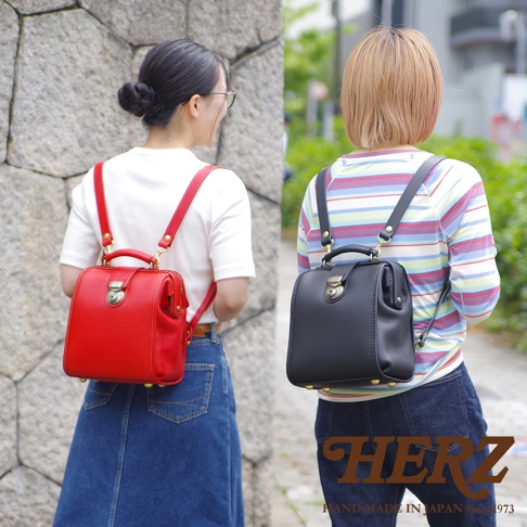 兩位女性各背著一個職人手作皮革迷你後背醫生包，左邊為鮮紅色，右邊為黑色。包款採用皮革材質，設計經典，帶有金屬鎖扣和提把。