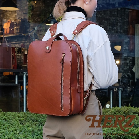 棕色皮革製成，方形設計的兩用後背包。正面有一個垂直拉鍊口袋，頂部有旋轉鎖扣和提把。肩帶為可調節式。