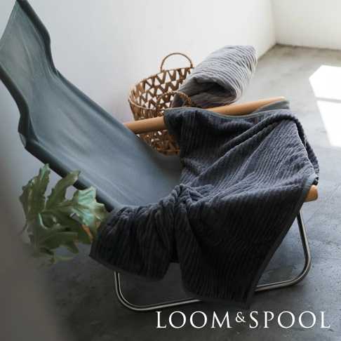 深灰色純棉立體直紋單人毯，質感微厚，柔軟舒適，搭配編織籃與簡約座椅，呈現溫馨居家氛圍。