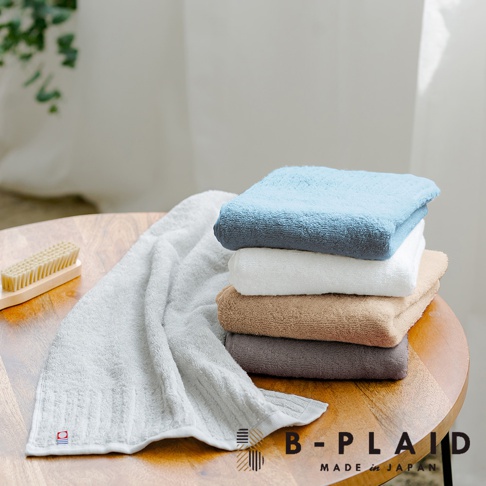一條淺灰色直紋毛巾攤開，旁邊堆疊著四條不同顏色的毛巾：淺藍色、白色、淺棕色和深灰色。毛巾質地蓬鬆柔軟，呈現長毛的質感。