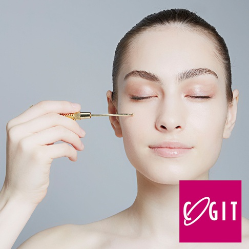 一位年輕女性的臉部特寫，她閉著眼睛，一手拿著一支金色、細長、末端帶有滾珠的美容工具，輕觸臉頰。