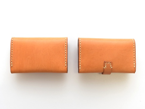 兩個簡約風格的淺棕色皮革名片夾，均以手工縫線裝飾，其中一個名片夾帶有皮質束帶開合設計。