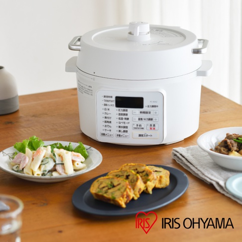 白色電子壓力鍋，帶有黑色控制面板，上面印有日文菜單和數字顯示。鍋蓋上有一個圓形提手。旁邊有一盤義大利麵沙拉和一盤日式煎蛋捲。