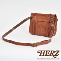 復古棕色皮革郵差包，具有水洗加工質感，配有可調節的長肩帶和金屬扣環，包身設計簡潔，帶有品牌標誌。