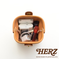 職人手作皮革口金化妝包 KF-143 S，呈現自然的淺棕色皮革，內部裝有手機、充電器、充電線和口紅等小物。