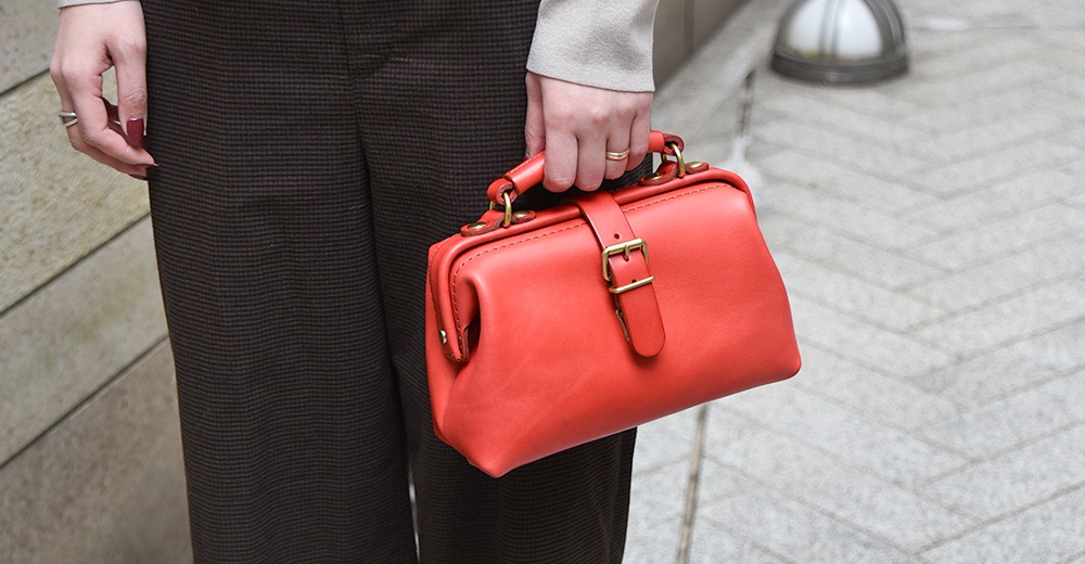 紅色皮革迷你手提包，帶有金色搭扣和提把，由職人手工製作。