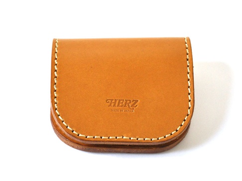職人手作皮革馬蹄造型零錢包，採用天然皮革製成，顏色為溫潤的棕褐色，縫線細緻，正面壓印有「HERZ」品牌標誌及「MADE IN JAPAN」字樣，設計簡約實用。