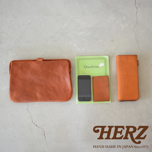 職人手作皮革Organ手拿包 G-38，共有三種尺寸與三種顏色。圖片中展示的是一款咖啡色皮革手拿包，搭配綠色筆記本、手機及同色系皮革卡夾。