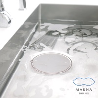 一個圓形淺灰色矽膠水槽蓋，置於濕潤的鋼製水槽中，周圍有泡沫和濾水器。