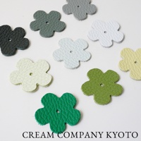 九個皮革製成的五瓣花形裝飾，顏色包含黑色、深綠、淺綠、淺黃、淺灰、白色和米白色，中央有小孔，散佈於白色背景上。