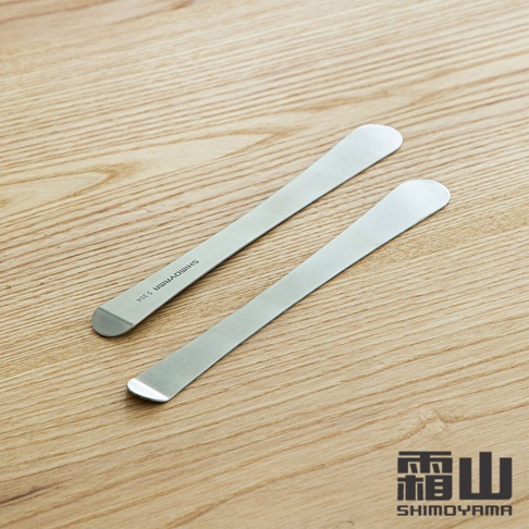兩支銀色 304 不鏽鋼長柄包餡勺/抹刀，呈對角線排列於木紋背景上。其中一支勺柄上印有「SHIMOYAMA S304」字樣。