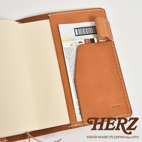 職人手作皮革手帳書套，淺棕色皮革，內有卡片夾層，壓印有HERZ品牌標誌與日文製造資訊。