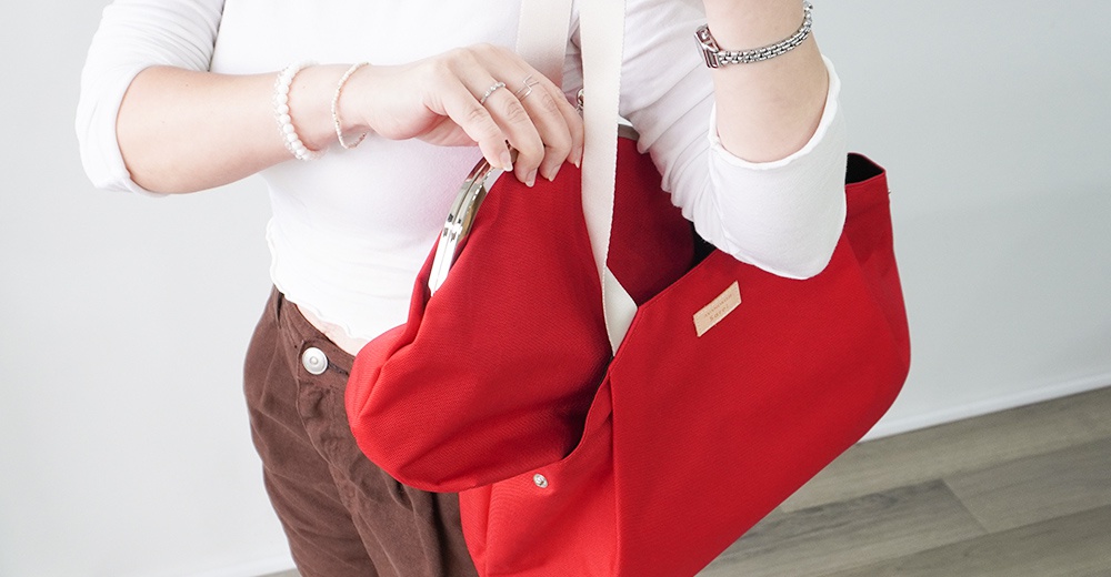 一位女性手持紅色 AYANOKOJI 托特包，包包上有品牌標籤，並配有白色背帶。