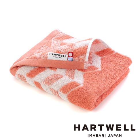 一條珊瑚橙色與白色相間的毛巾，以傳統和風紋樣織成，質感柔軟，帶有 HARTWELL IMABARI JAPAN 的標籤。