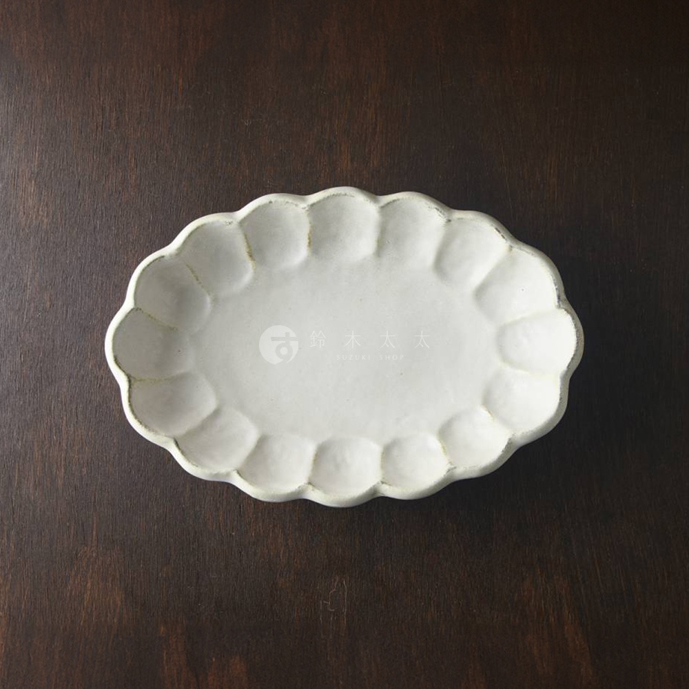 一個淺灰色的、帶有花型邊緣的橢圓形陶瓷料理盤，盤面有細微的紋理，擺放在深色木質背景上。