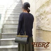 一位女士斜背一個黑色皮革復古口金兩用手提包，包包上有金色金屬配件和提把，整體呈現簡潔的設計風格。