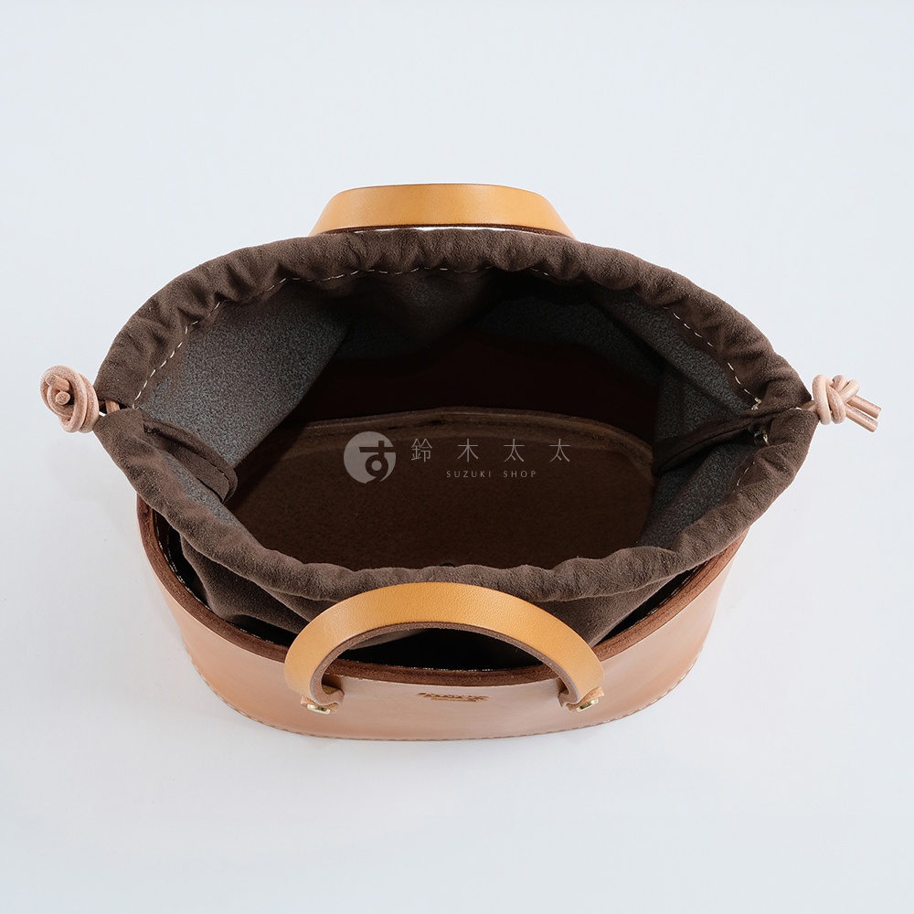 職人手作皮革束口手提包，淺棕色皮革外觀，內襯為深棕色布料，束口處有粉色細繩，雙提把設計。