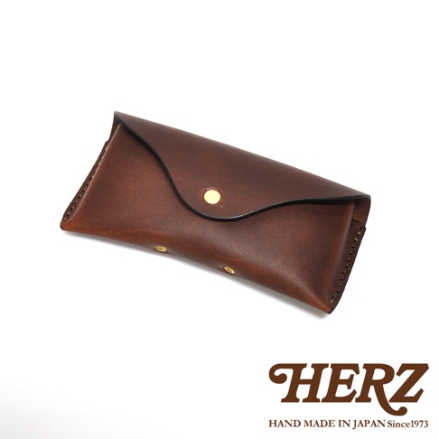 一個棕色皮革眼鏡收納盒，帶有金色鉚釘和品牌標誌。