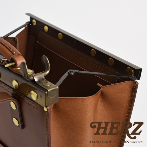 職人手作皮革復古口金後背包，展現皮革的自然紋理與光澤，搭配黃銅色金屬扣環與結構，設計簡約大方。