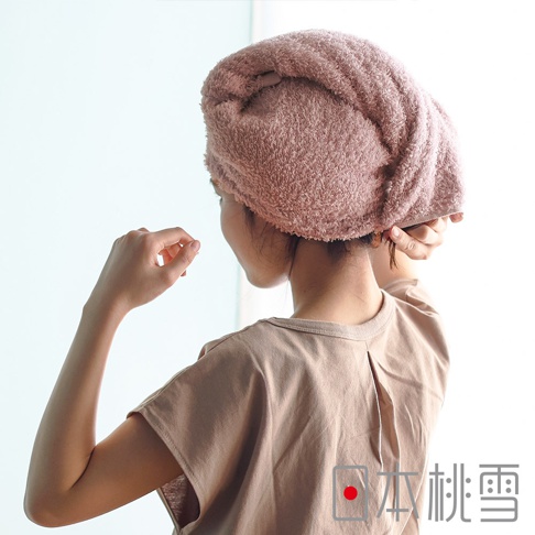 女性穿著淺棕色上衣，頭戴粉色吸水毛巾，從背後拍攝。