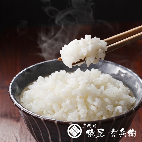 一碗熱騰騰的北海道夢美人米，米粒飽滿潔白，散發著誘人蒸汽。筷子夾起一撮米飯，展示其顆粒分明的質地，碗身為深灰色帶有條紋設計。