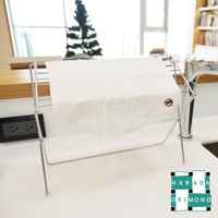 白色八重紗精繡萬用吸水擦拭巾，柔軟細緻，帶有棕色與黃色的小圖案刺繡，置於銀色金屬架上，背景為明亮的居家環境。